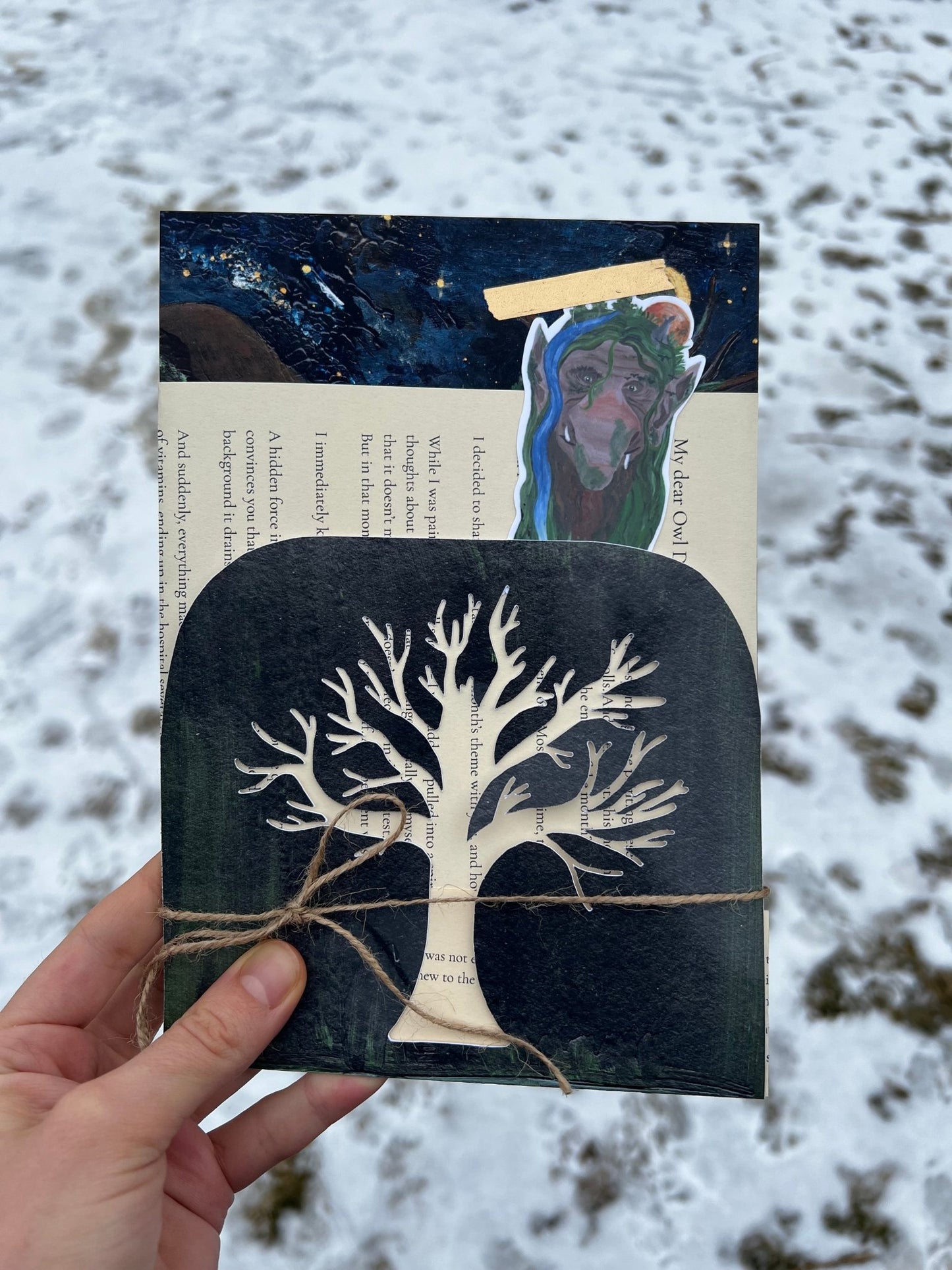 Hand holding a book with a tree design against a snowy background