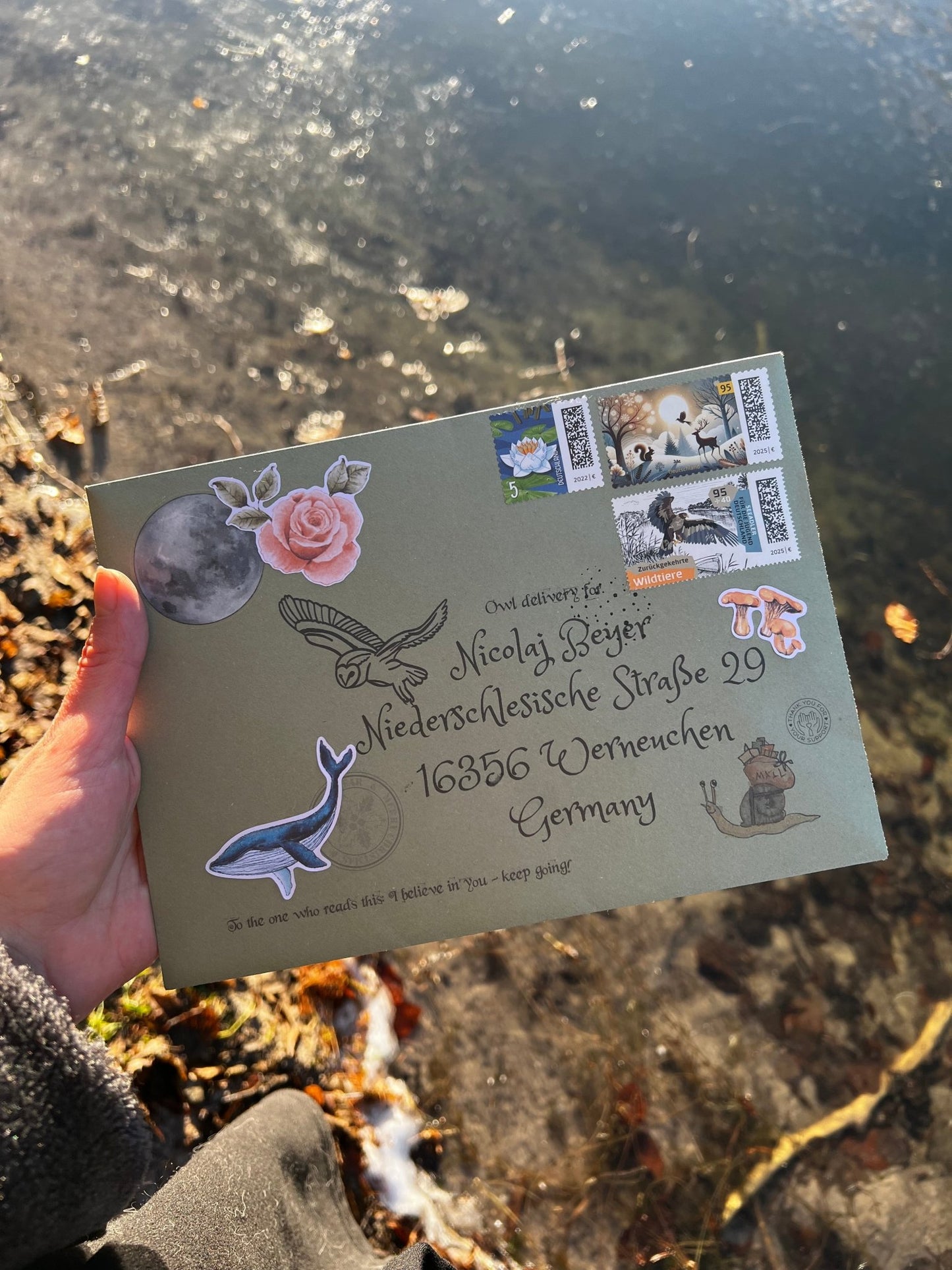 Hand holding a decorative envelope with stamps and stickers against a natural background