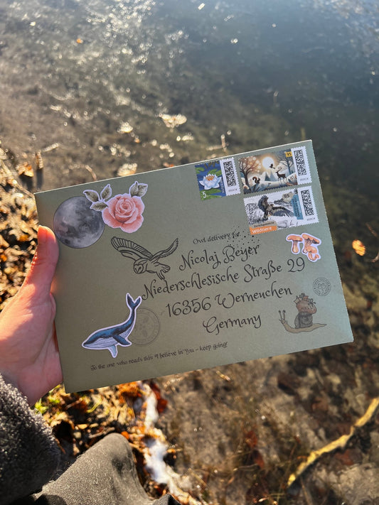 Hand holding a decorative envelope with stamps and stickers against a natural background