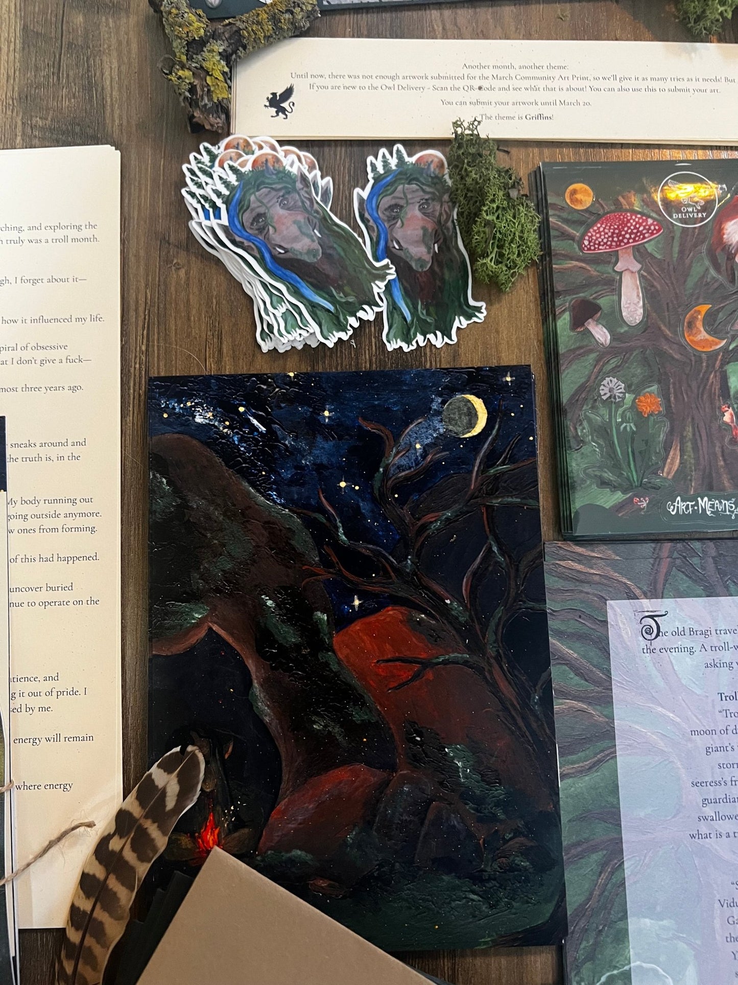 Stickers and artwork on a wooden surface with books and feathers.