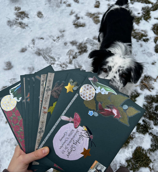 Hand holding a stack of decorated cards with a dog in the background on a snowy ground